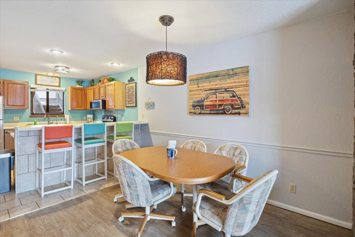 A vibrant dining area with a family-sized table, colorful bar stools, and a view of the kitchen. The space exudes warmth and is clearly designed for shared meals, casual gatherings, and cooking together.