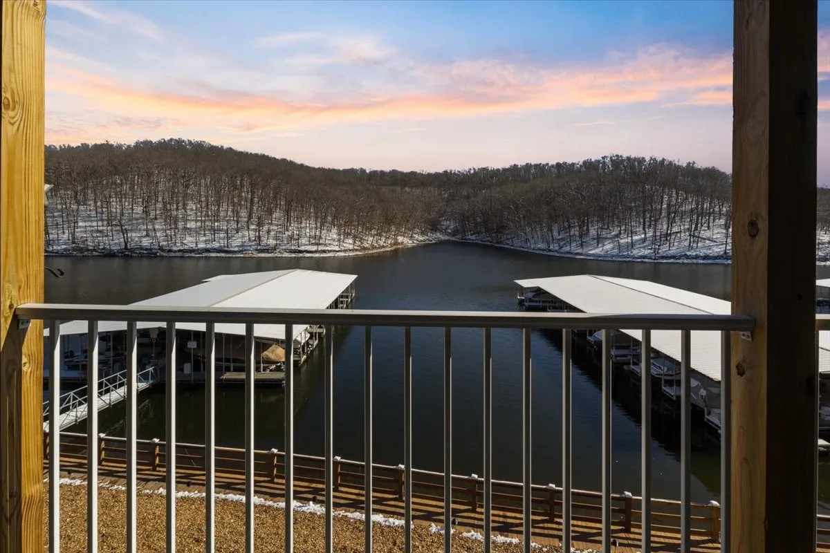 This image captures a tranquil lakeside scene featuring a dock extending into the water, snow-covered hills in the background, and a dramatic sunset sky. The dock provides a clear sense of access to the lake for activities like kayaking and fishing, while the peaceful water and sunset evoke the natural beauty of the area.