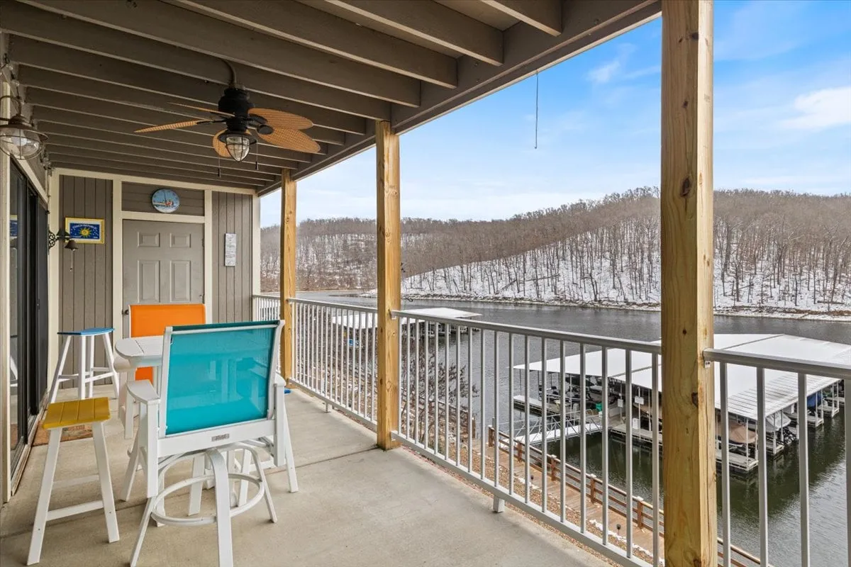 A vibrant outdoor setting with colorful furniture on a balcony overlooking the water and marina docks, framed by distant snow-capped hills. The space radiates leisure and provides a scenic spot for socializing, reading, or simply taking in the lakeside views.