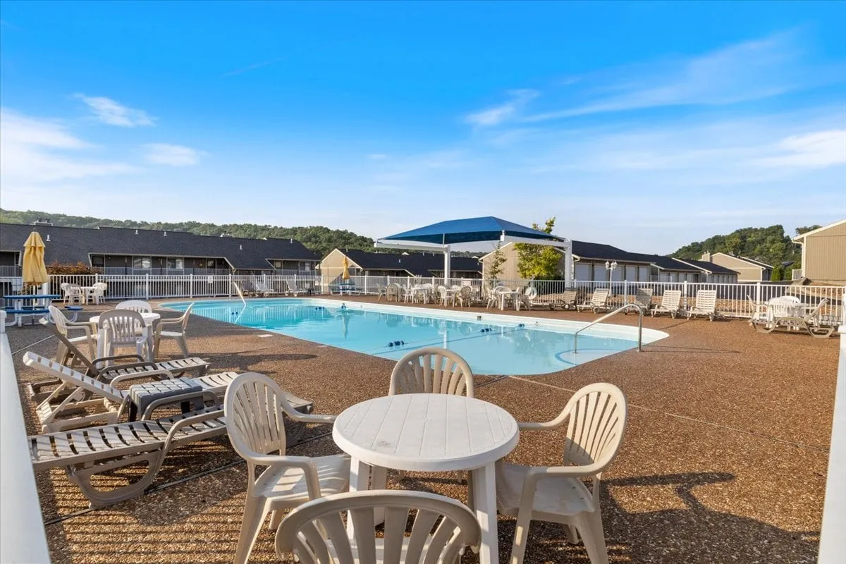 A sparkling resort-style swimming pool surrounded by comfortable lounge chairs, umbrellas, and a table for group gatherings. The area is spacious, inviting for both swimming and socializing, and hints at leisure and fun under the sun.