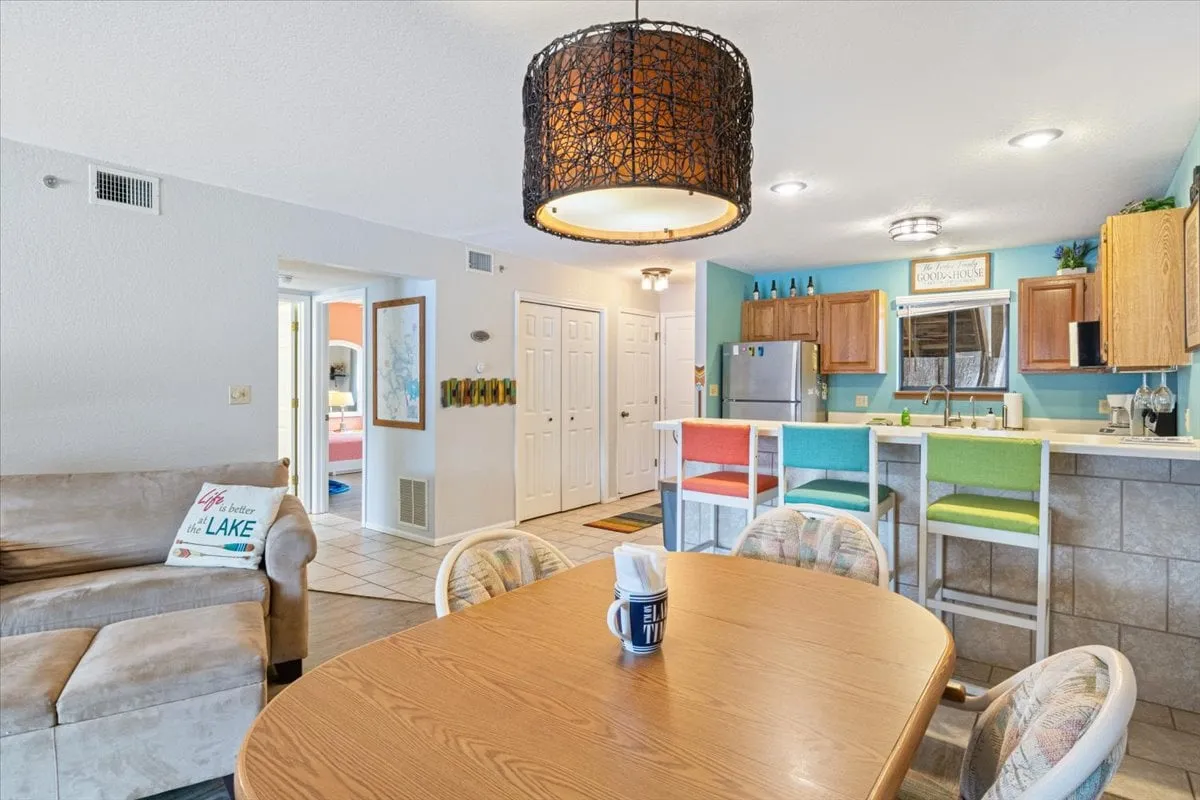 A round dining table, cheerful bar stools, and visible kitchen cabinetry in a bright, inviting setting. Decorative lighting and practical layout hint at a space that's ideal for brunches, coffee breaks, and casual family gatherings.
