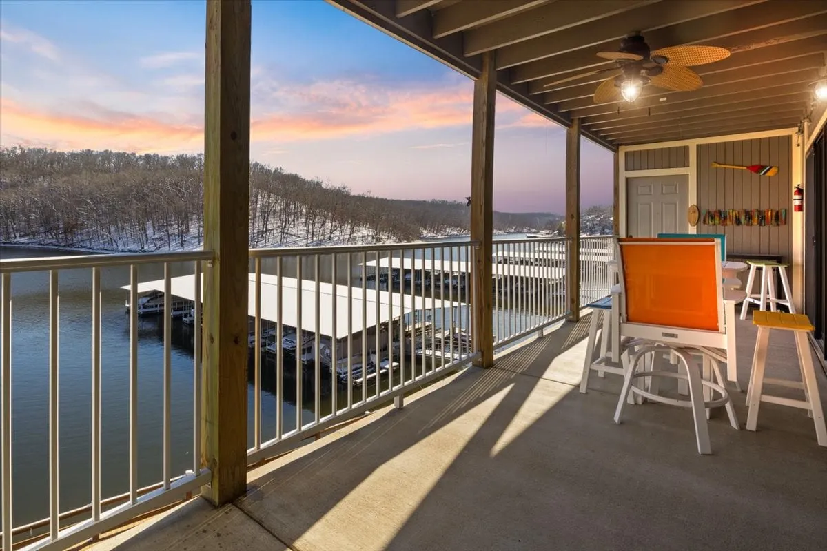 A peaceful lakeside balcony with a railing, a painted easel set up for painting, and a sweeping waterfront view framed by distant hills. The setup hints at creative inspiration or restful contemplation, while the outdoor setting underscores access to nature.