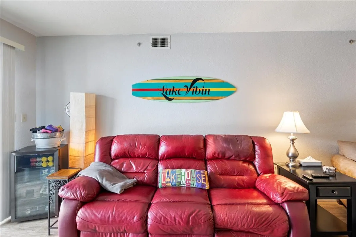 A casual and inviting living space with a red leather sofa, decorative surfboard, lamp, and coffee table. The room is set up for relaxation, socializing, and game nights, with décor that hints at a fun, lakeside lifestyle.