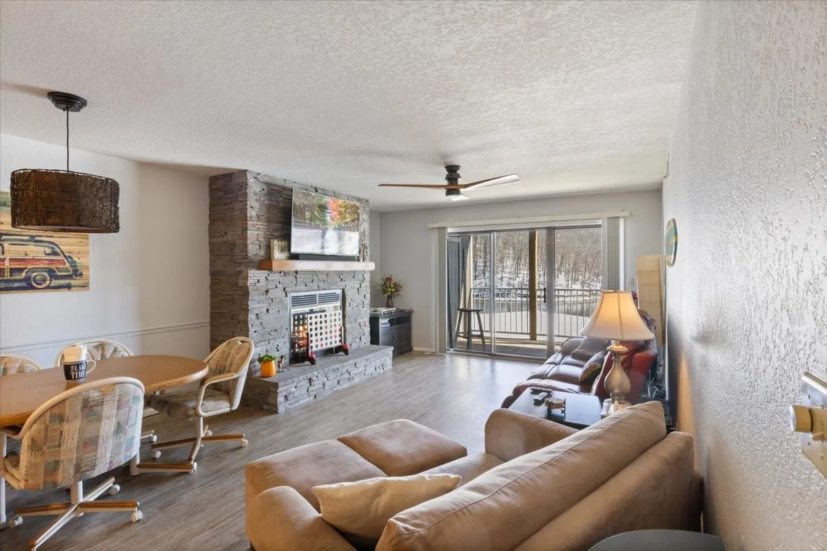 A warm and welcoming open-plan living and dining area featuring a stone fireplace, comfortable seating, a dining table, and large windows that let in natural light. The space is designed for social gatherings, relaxation, and enjoying the view.